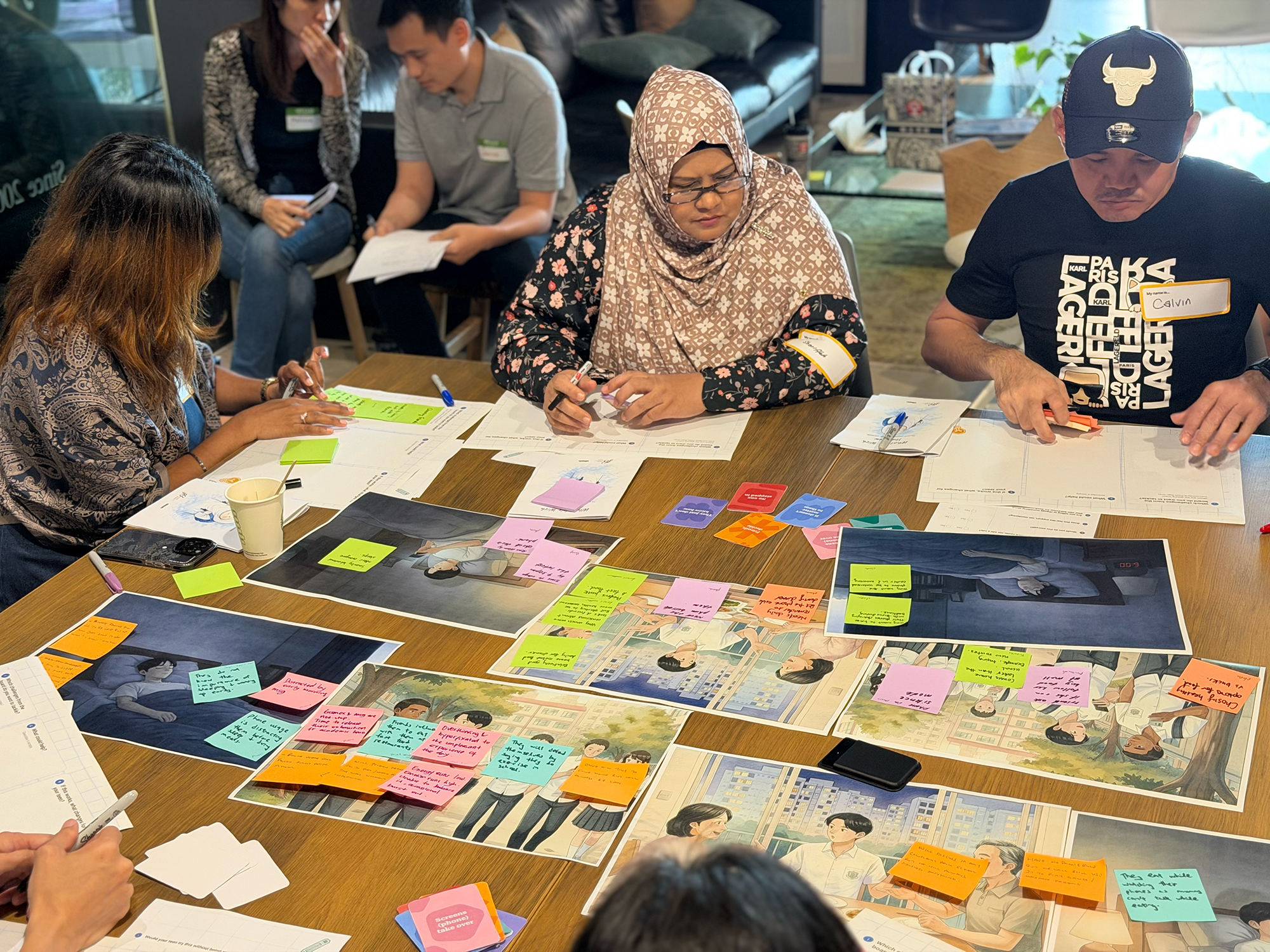 Parents during co-creation workshop — writing on sticky notes with scenario cards and illustrations spread on table